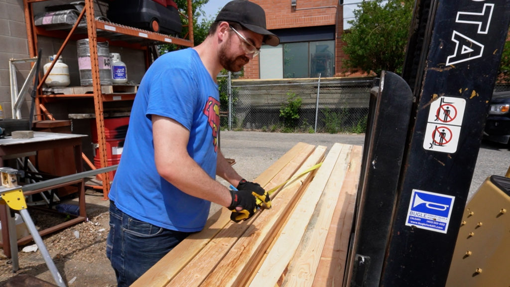 A man uses a measuring tape on a pile of wood.