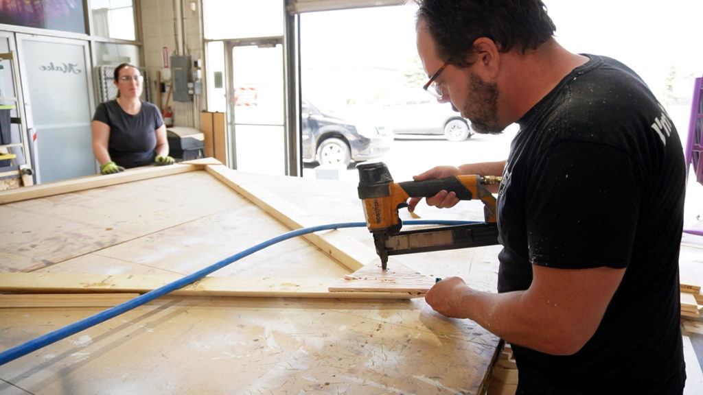 Two volunteers work on a wooden triangle for the 2023 Freezer Burn Effigy.