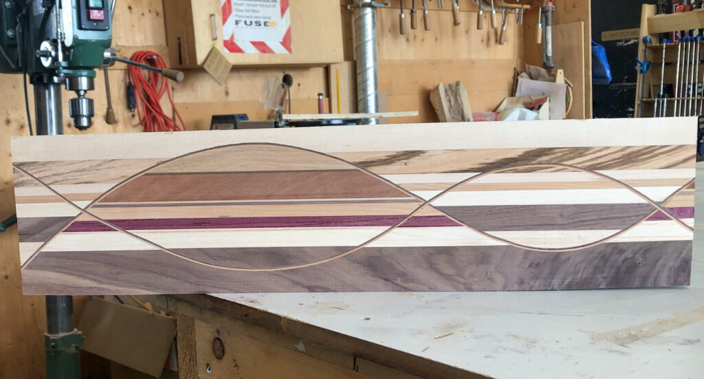 A intricate piece of wood with curved inlays sits in a woodshop.